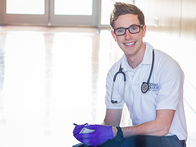 Zach Gibson, an alumni, wearing gloves and a stethoscope.