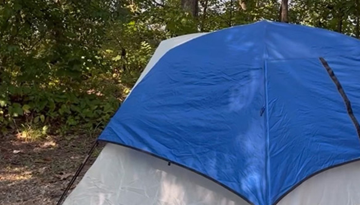 a blue and white tent sits on the ground in front of trees