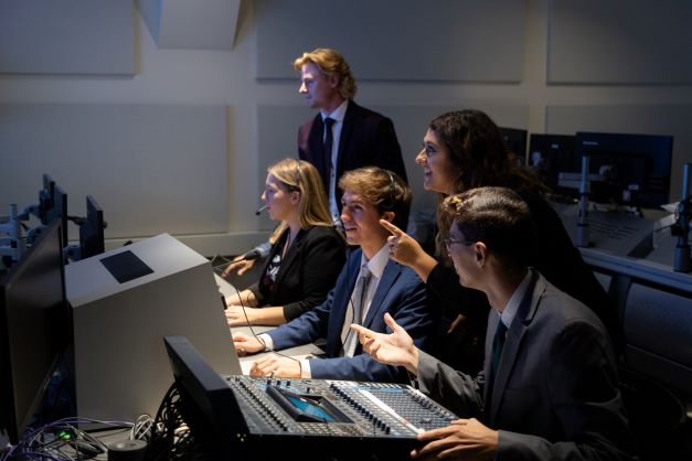 Five students huddle around a computer screen. One female student points towards it.