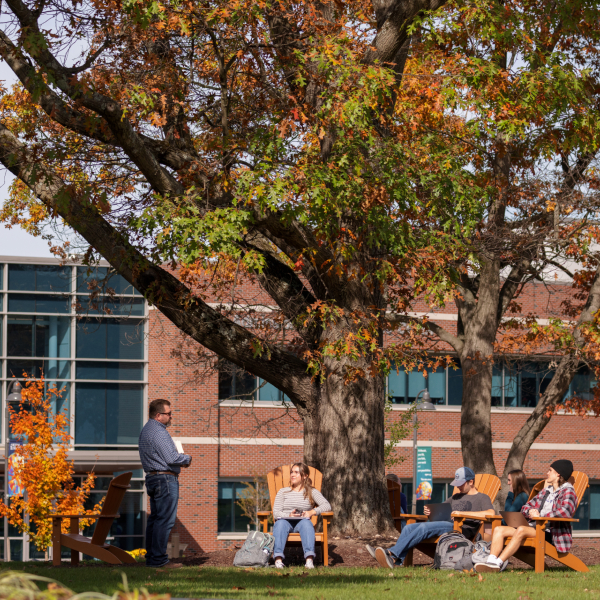 Fall on campus, students outside sitting in adirondack chairs.