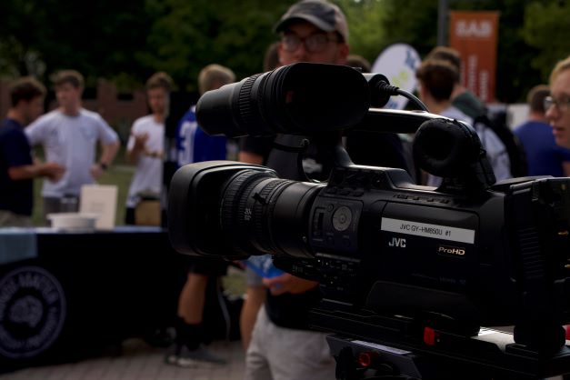 A close-up of a camera sitting outside, filming people.