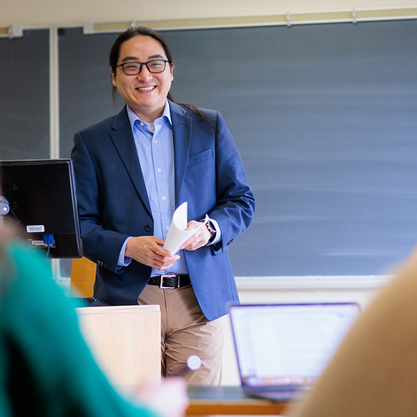 Jason Renn stands in front of a classroom, wearing a navy blazer.