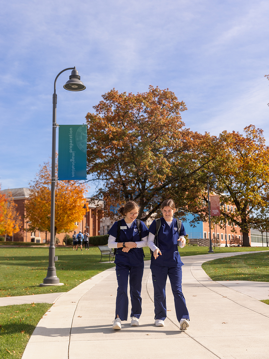 Two nursing students walk down a sidewalk on Messiah's campus. They are walking toward the camera.