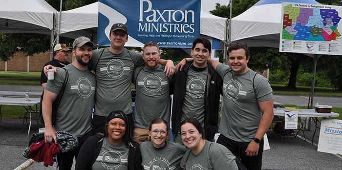 A group of students stand in front of a Paxton Ministries sign