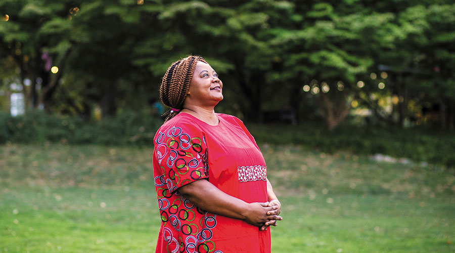 Photo of middle aged immigrant black woman in red outfit looking up to the sky