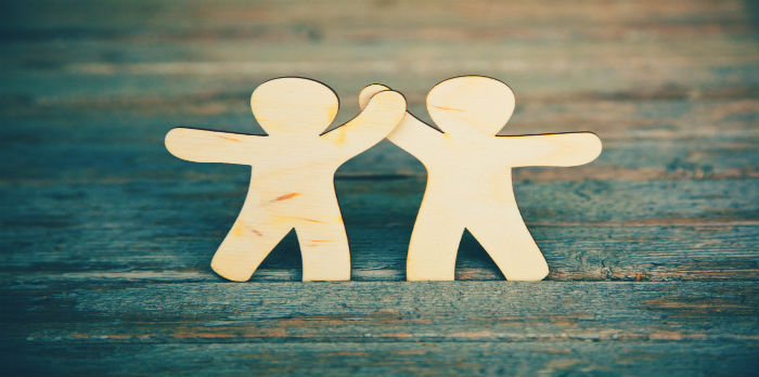 A photo of two wooden figures giving each other a high five with a dark background.