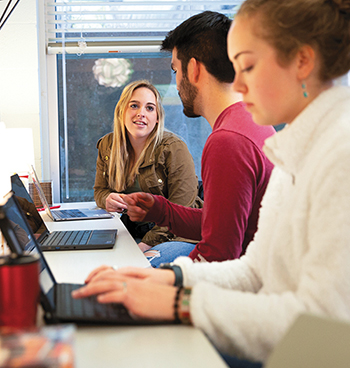 Three students sitting at a table on their laptops