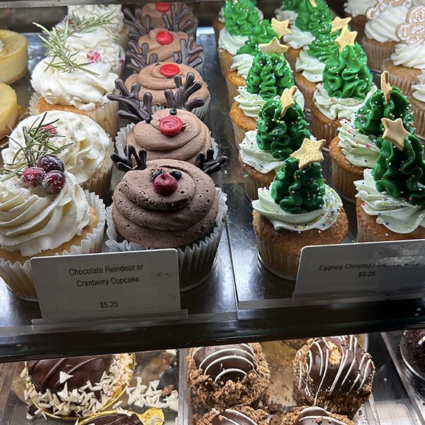 Cupcakes sit in a glass case, decorated as a reindeer and Christmas trees.