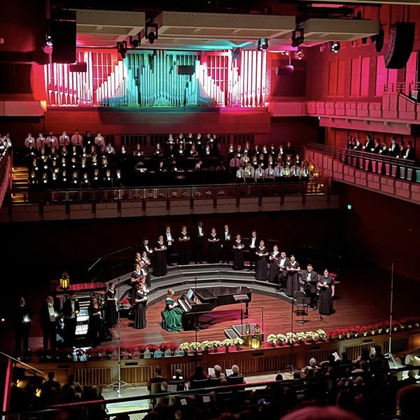 Students dressed in all black stand on stage during a Christmas concert. The lights behind them are green and red.