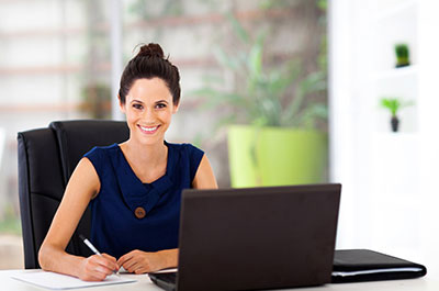 Attractive woman at office desk writing on paper with a laptop infront