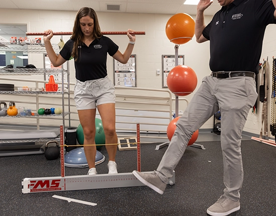 A professor works with a female athletic training student on exercises in the lab.
