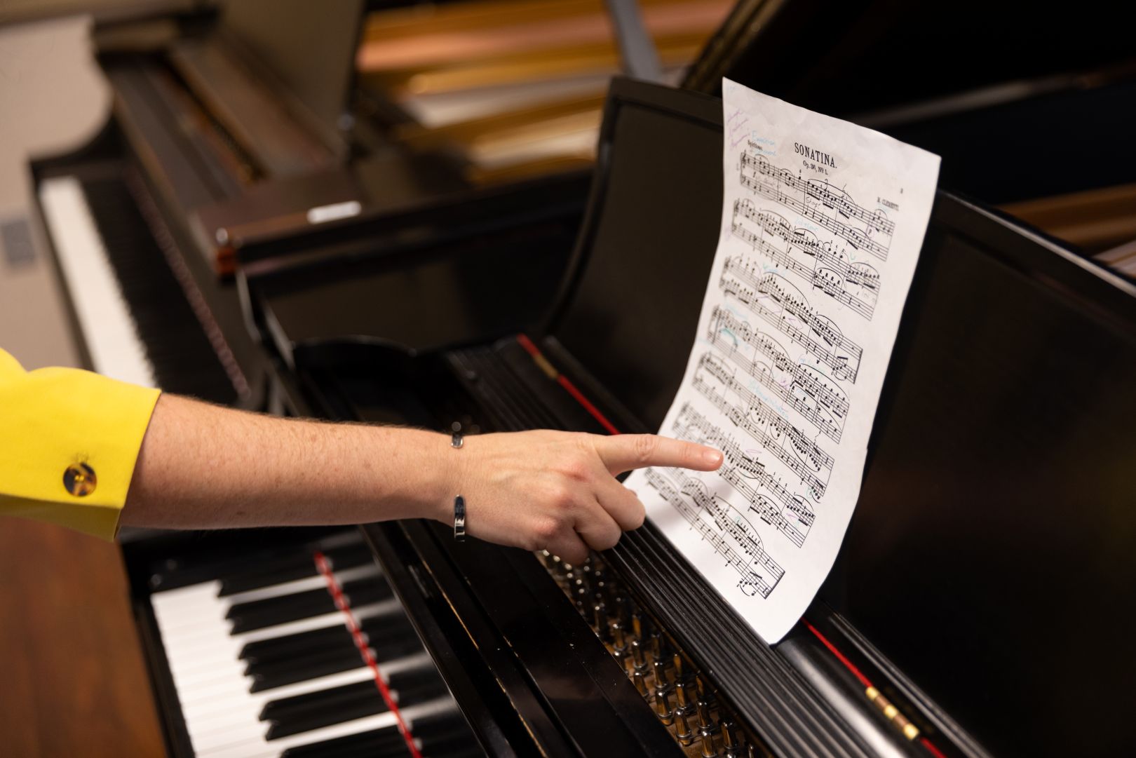 A hand pointing sheet music on a piano. 
