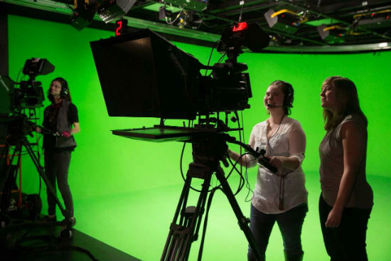 Students use cameras in front of the production studio green screen