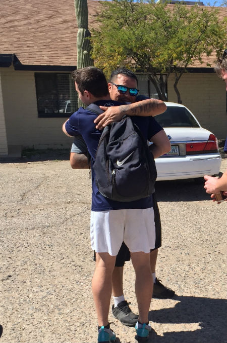 Two men stound outside embracing one another.