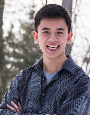 A young man smiles outside in front of winter trees.