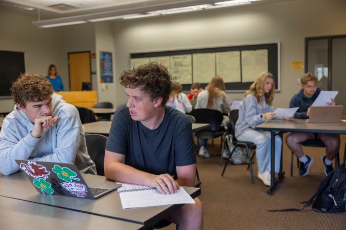 Student helping another student with homework at a desk. 