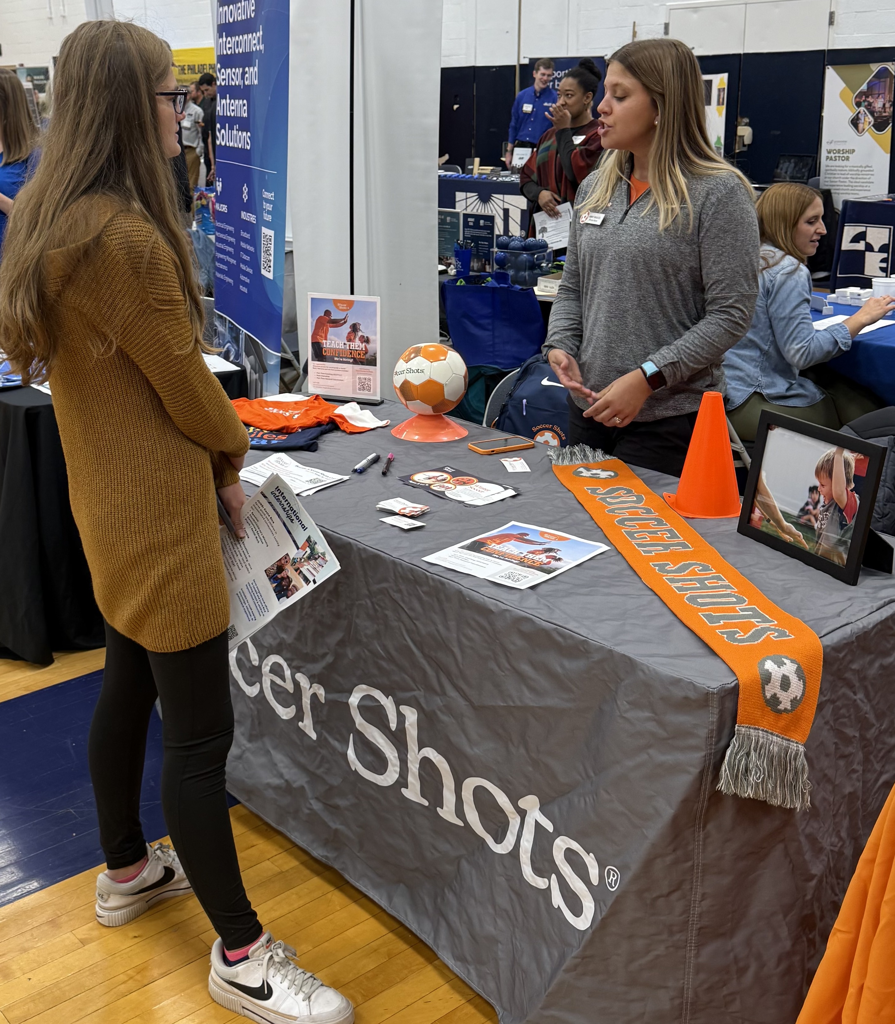 A young woman standing in front of a table talking