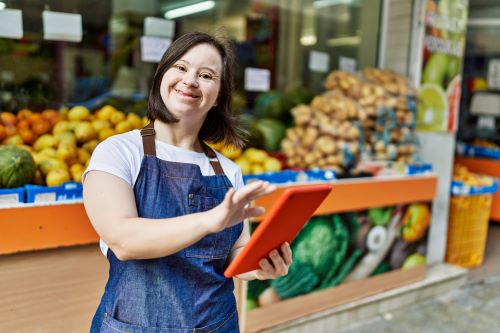 A young woman on a tablet in front of a fruit stand. 