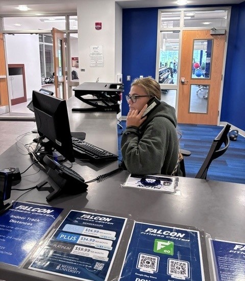A young woman sitting at a desk answering a telephone call. 