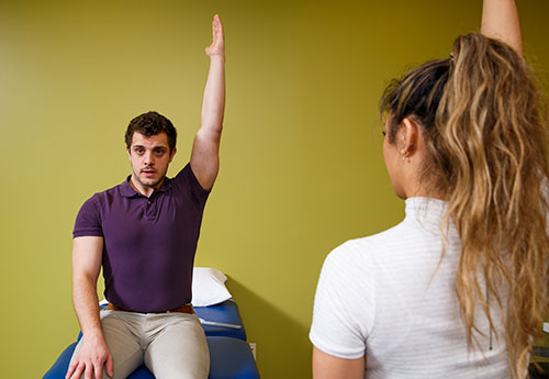 Man raising arm above head as physical therapist assists