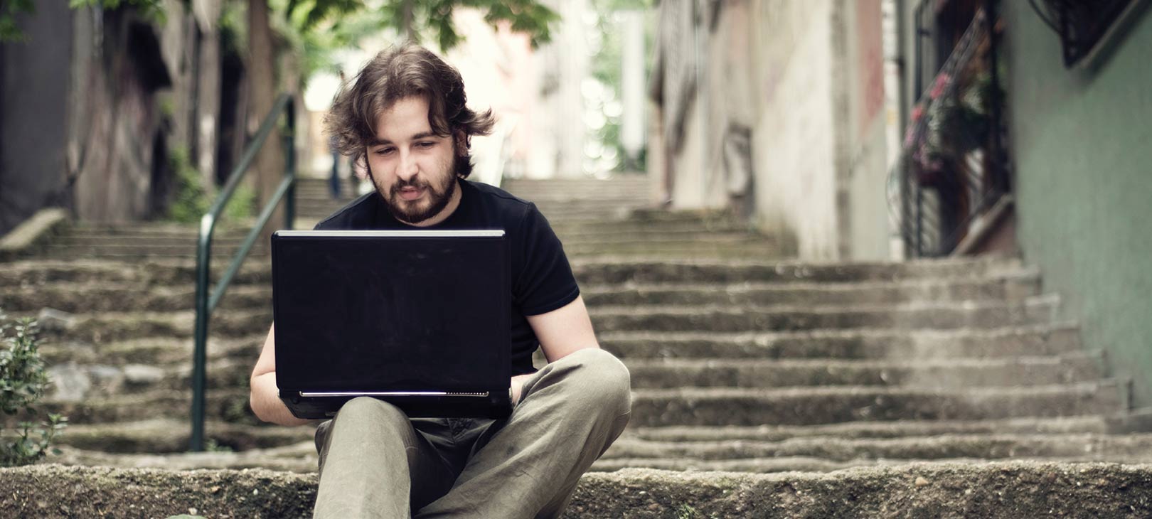 Undergrad Online A male caucasian student sitting on stairs with a laptop.jpg