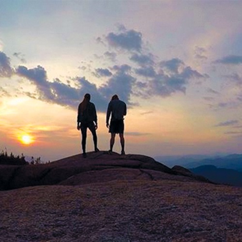 Two people standing on mountain at sunset