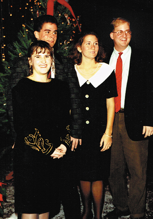 A group of four people dressed in formal attire posing together in front of a decorated Christmas tree.