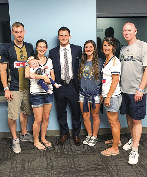 A family poses together with a soccer player, wearing Philadelphia Union jerseys, in a casual setting.