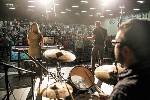 A live music performance featuring musicians on stage and an audience engaged in a large venue.