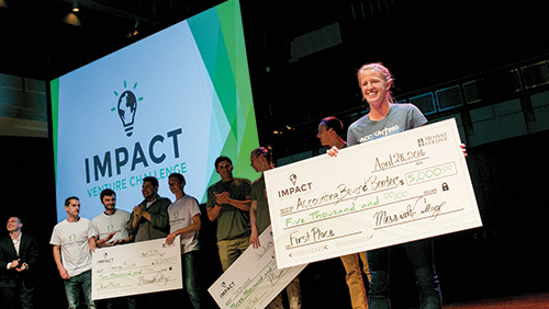 Participants holding oversized checks at the IMPACT Venture Challenge awards ceremony, showcasing the winning team with a logo in the background.