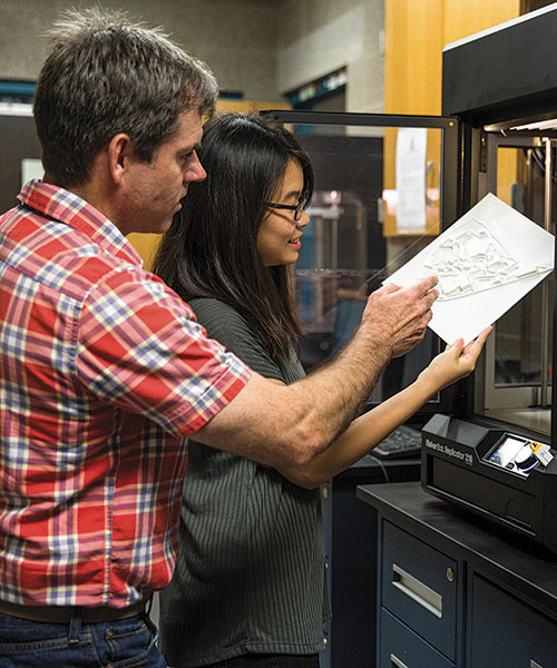 Two individuals examining a 3D printed object in a workshop setting.