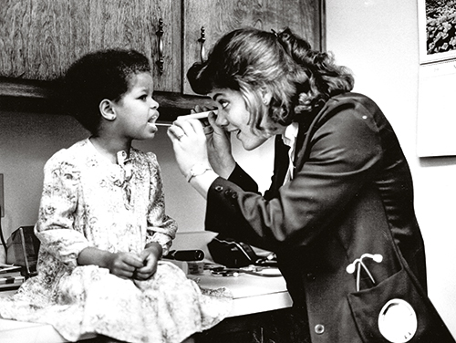 A black and white photo of a nurse examining a child in 1984