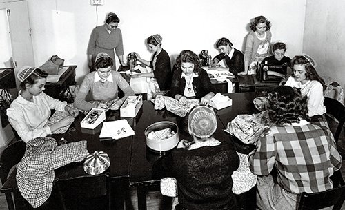 Historical photograph of women engaged in sewing activities, showcasing their skills and collaboration in a workshop setting.