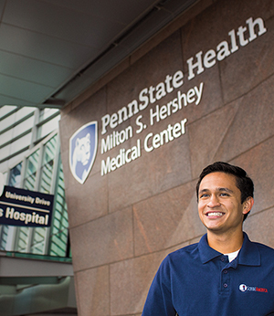 Man stands in front of Penn State Hershey Hospital smiling