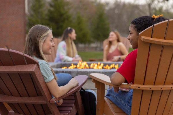 two women sitting next to the on-campus firepit and talking
