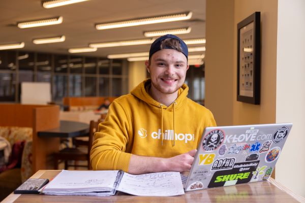 male student in yellow sweatshirt with laptop