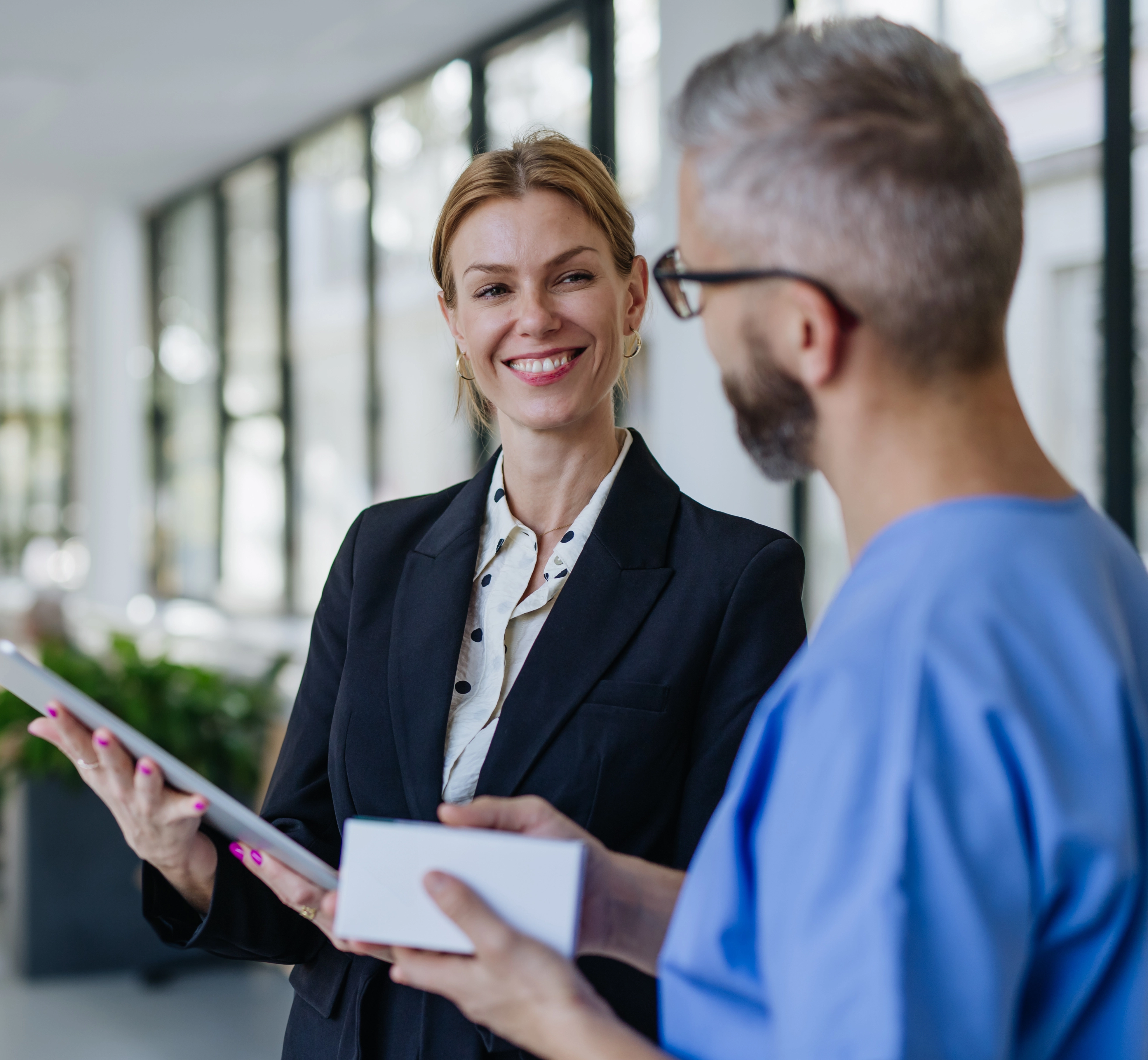 A professionally dressed woman speaks to what appears to be a doctor in a hallway