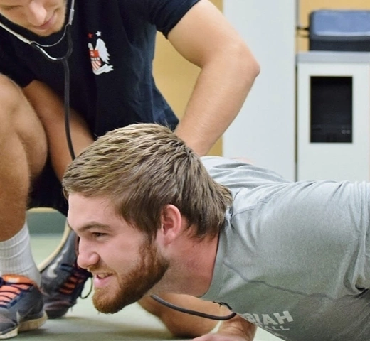 Male student doing push-ups with student trainer