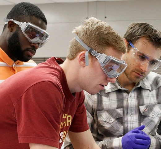 Three male students wearing safety glasses in a classroom lab