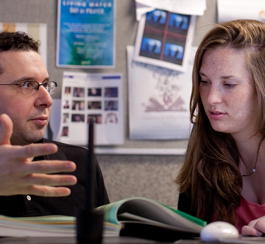 professor talking to student with a book open