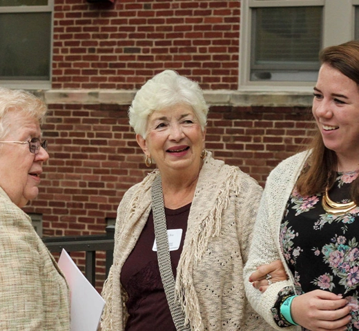 A small group of generationally diverse women greet each other outside a campus building.