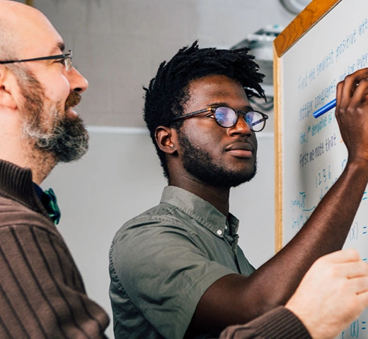 Student and professor working on a math problem on a white board.