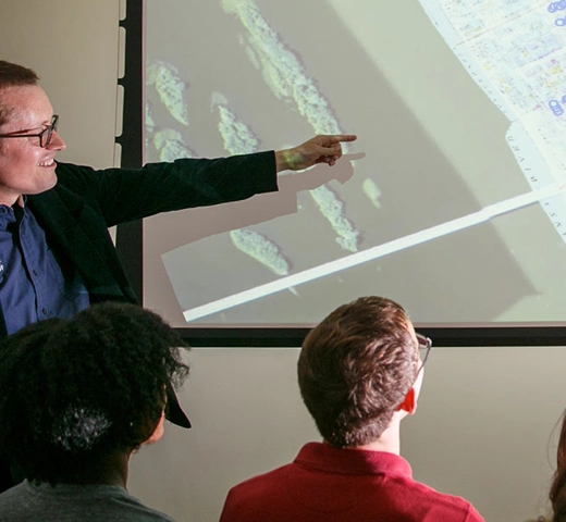 Professor pointing at a slideshow to students in a class