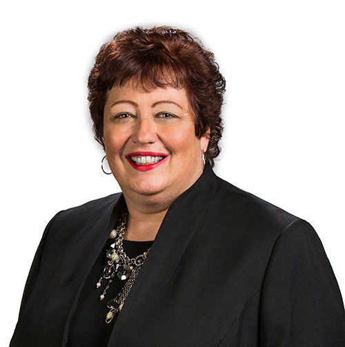 A woman wearing a black blazer and jewelry smiles in a professional headshot against a white background.