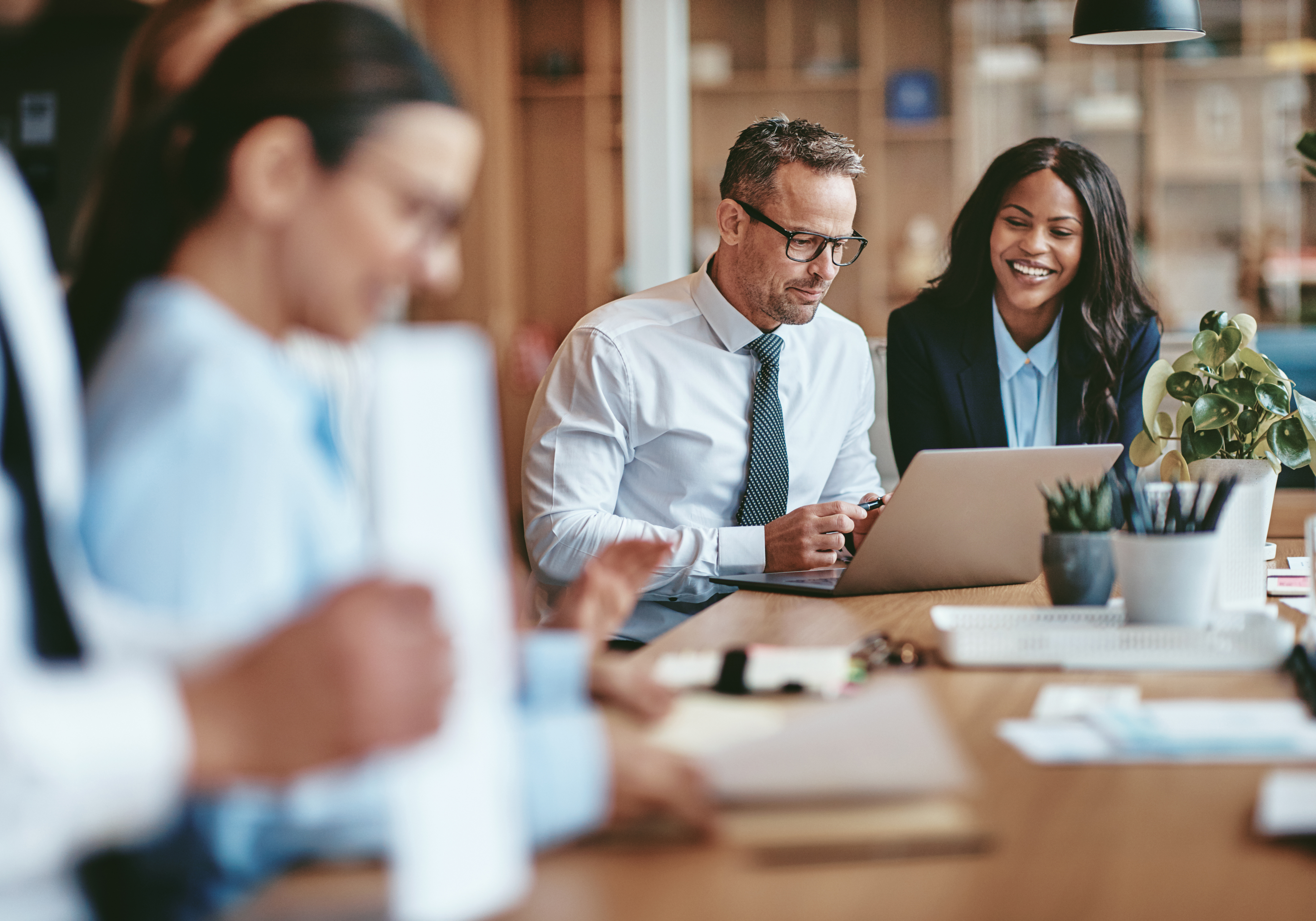 A group of professionals collaborating in a modern office setting, with one individual working on a laptop while others engage in discussion.
